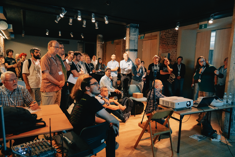 A group of people watching a 2-minute presentation during the opening of the exhibition of practitioners and industry demos